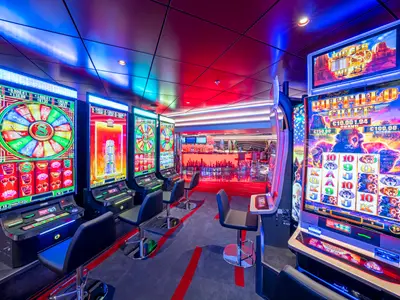 Blick in das farbenfroh beleuchtete Casino an Bord der MSC Seascape. Zahlreiche moderne Spielautomaten und eine elegante Bar im Hintergrund laden zum Spielen ein.