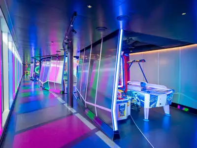 Moderner Arcade-Spielbereich an Bord der MSC Seascape mit Airhockey und Videospielen. Leuchtende Pink- und Blaulichter reflektieren auf dem Boden.