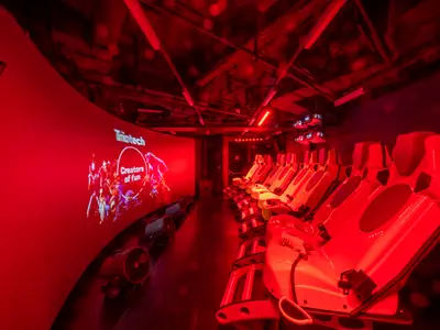 Ein interaktives XD Cinema an Bord der MSC Seascape, beleuchtet in intensivem Rot. Mehrere Reihen futuristischer Sitze sind in einer Kurve angeordnet und zeigen auf eine grosse Leinwand mit der Aufschrift "Creators of fun". Die Decke zeigt sichtbare Rohre und eine moderne Lichtinstallation. Keine Personen sind zu sehen.