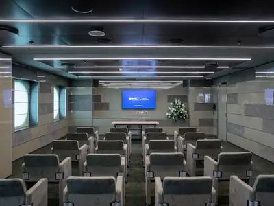 Konferenzraum an Bord der MSC Seascape mit Reihen grauer Sessel, Podium und Bildschirm. Stilvolle Wände und LED-Lichtleisten.