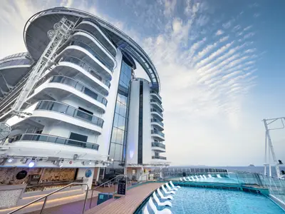 Blick von unten auf das schneeweiße Heck der MSC Seascape mit Infinity Pool, angrenzender Gelateria und Glasfassade unter blauem Himmel und Wolkenformationen.