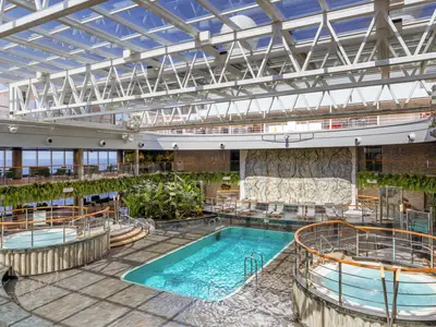 Blick auf den lichtdurchfluteten Jungle Pool der MSC Seascape. Ein grosser Pool, zwei Whirlpools, viele Pflanzen, Liegen und Meerblick.