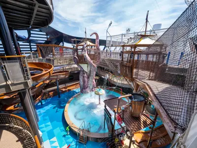 Blick auf den Pirates Cove Aquapark an Bord der MSC Seascape. Zu sehen sind Wasserrutschen, ein Planschbecken mit Oktopus-Skulptur und ein Abenteuerparcours mit Seilnetzen unter blauem Himmel.