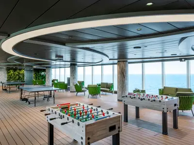 Moderner Sport- und Loungebereich an Bord der MSC Seascape mit Tischtennis, Kickertischen und grünen Sitzgelegenheiten. Große Fenster bieten Meerblick.
