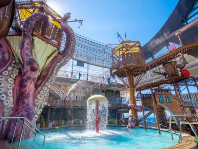 A lively water park on the MSC Seascape cruise ship, with giant purple octopus tentacles, a pirate ship play structure, and a mushroom water fountain.