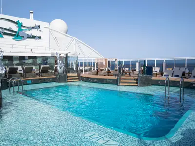 Pooldeck der MSC Seascape. Grosser Aussenpool umgeben von Holzdecks und Liegestühlen. Silberne Meerjungfrauen-Skulpturen zieren den Bereich. Blick auf das offene Meer.