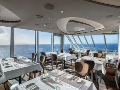 Panoramablick auf das elegante MSC Yacht Club Restaurant an Bord der MSC Seascape mit Tischen, Stühlen und weitem Meerblick.