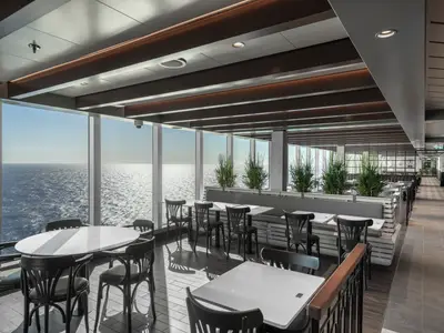 Ein helles Buffetrestaurant an Bord der MSC Seascape mit modernen Tischen und Stühlen. Grosse Fensterfront bietet weiten Blick auf das glitzernde Meer und den Horizont.
