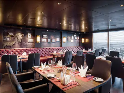 Ein luxuriöses Steakhouse, Butcher's Cut, an Bord der MSC Seascape. Dunkle Ledersessel und rote Banketten, elegant eingedeckte Tische und dekorative Wandbilder mit Rindermotiven sind zu sehen.