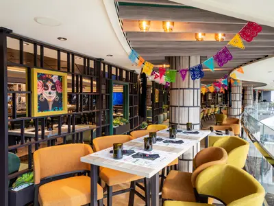 Blick in das bunte mexikanische Spezialitätenrestaurant Hola! Tacos & Cantina an Bord der MSC Seascape, mit Tischen und orangefarbenen Stühlen, geschmückt mit farbigen Wimpelketten und Kunstwerken.