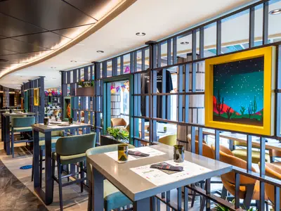 Das Spezialitätenrestaurant Hola! Tacos & Cantina an Bord der MSC Seascape. Moderne Tische, Stühle und dekorative Trennwände mit bunter Kunst und Lichterketten.