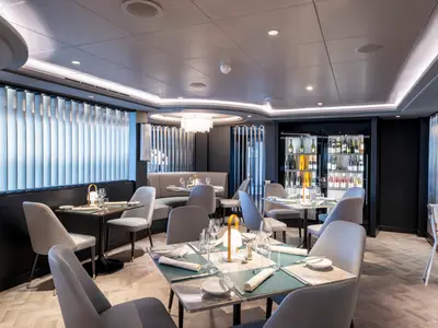 Ein modernes und elegantes Restaurant an Bord der MSC Seascape. Es sind Tische, Stühle, Gedecke und eine beleuchtete Weinauslage zu sehen. Das Ambiente ist chic.