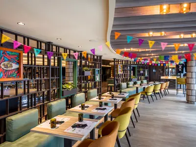 Hola! Tacos & Cantina Restaurant an Bord der MSC Seascape. Bunte Girlanden und mexikanische Kunst. Gruene Sitzbaenke und gelbe Stuesseln.