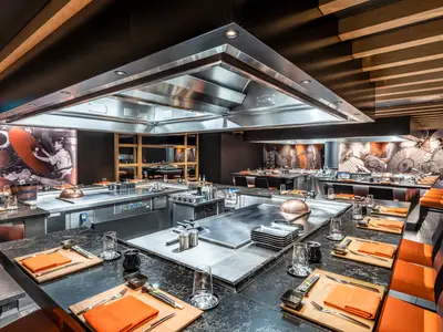 Kaito Teppanyaki Restaurant an Bord der MSC Seascape. Moderne Kochstationen, Tische mit orangefarbenen Stühlen und japanische Wandkunst.