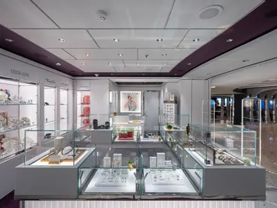 Moderner, heller Schmuck-Shop an Bord der MSC Seascape. Glasvitrinen zeigen elegant Ketten, Ringe, Uhren. Violette Deckenakzente und ein Swarovski-Plakat sind sichtbar.