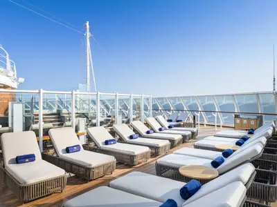 Ein sonniges Deck an Bord der MSC Seascape mit Reihen von Liegestühlen, blauen Handtüchern und Panorama auf das offene Meer unter blauem Himmel, umrahmt von Glasgeländern.