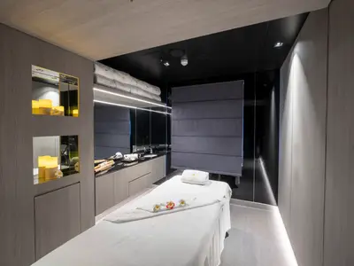 Modernes Spa an Bord der MSC Seascape. Ein Behandlungsraum mit weisser Massageliege, Waschtisch und beleuchteten Nischen mit Kerzen.