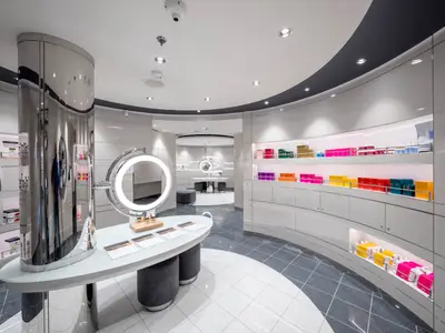 Elegante Spa-Verkaufsfläche an Bord der MSC Seascape. Geschwungene weisse Wände, beleuchtete Regale mit bunten Wellnessprodukten, grosse Spiegel, gemusterter Boden.