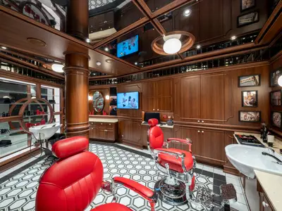 Barbershop der MSC Seascape. Klassische Holztäfelung, rot-silberne Friseurstühle, Schachbrettboden, Spiegel, Bildschirme.