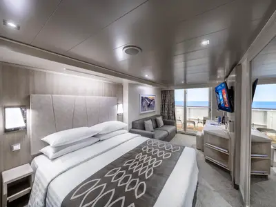 Eine moderne, helle Balkonkabine an Bord der MSC Seashore mit einem großen Doppelbett, einer Sitzecke mit Sofa und einem Balkon mit Meerblick.