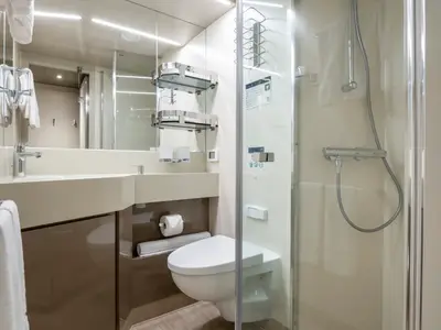 Das moderne Badezimmer einer Balkonkabine an Bord der MSC Seashore mit Waschtisch, Toilette und Glasduschkabine. Helle Beleuchtung und minimalistisches Design dominieren.