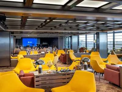 Einladendes Brooklyn Café an Bord der MSC Seashore mit bequemen gelben Sesseln und dunklen Tischen. Im Hintergrund ist eine Bühne mit einem blauen Bildschirm und Musikinstrumenten zu sehen. Große Fensterfronten bieten Meerblick.