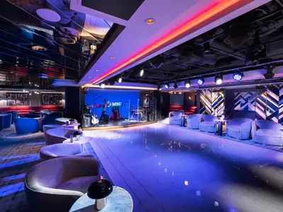 Die Uptown Lounge an Bord der MSC Seashore zeigt eine beleuchtete Bühne mit Instrumenten und eine Tanzfläche. Bequeme Sessel und Sofas im modern beleuchteten Innenraum.