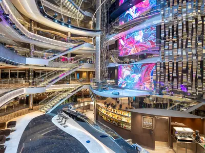 Modernes, mehrstöckiges Atrium der MSC Seashore. Breite Treppen, leuchtende LED-Bildschirme mit Blumenmustern und die Seashore Bar. Glas, Spiegel und Licht schaffen eine luxuriöse Atmosphäre.