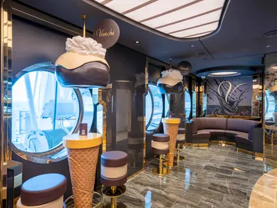 Die luxuriöse Venchi 1878 Chocolate Bar an Bord der MSC Seashore mit dunkler Einrichtung, goldenen Akzenten, thematischen Barhockern und Blick auf das Meer durch Bullaugen.
