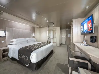 Eine helle, barrierefreie Kabine an Bord der MSC Seashore mit Doppelbett, Schreibtisch und sichtbarem Badezimmer. Moderne Einrichtung in Holz- und Grautönen.