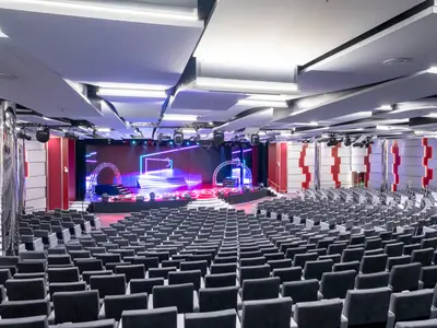 Ein weitläufiges Theater an Bord der MSC Seashore, gefüllt mit Reihen dunkler Sessel, vor einer modern beleuchteten Bühne mit blauen und lila Neonstrukturen und einem kreisförmigen Bogen.