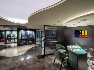 Kunstgalerie der MSC Seashore. Ausgestellte Schwarz-Weiss-Fotografien und Kunstwerke. Grüner Empfangstresen, "ART GALLERY"-Schild. Elegante Deckenbeleuchtung und gemusterter Boden.