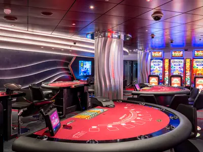Blick ins luxuriöse Casino an Bord der MSC Seashore mit mehreren roten Spieltischen und leuchtenden Slotmaschinen. Der Raum ist modern gestaltet mit Wellen-Lichtinstallationen an der Wand und Säulen.