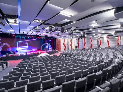 Weitwinkelaufnahme des Madison Theaters an Bord der MSC Seashore mit zahlreichen leeren Sitzreihen und einer futuristisch beleuchteten Bühne. Die Decke ist mit geometrischen Paneelen und Lichtern versehen.