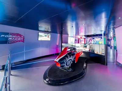 Blick in den "MSC Formula Racer" Bereich an Bord der MSC Seashore. Ein roter Rennsimulator steht im Zentrum, umgeben von Bildschirmen und Arcade-Automaten. Helle Beleuchtung und Neonstreifen schaffen eine lebendige Atmosphäre.