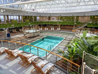 Überdachte Jungle Pool Lounge der MSC Seashore. Pool, Whirlpools, Liegen und tropische Pflanzen füllen den grosszügigen Bereich. Blick auf das Meer durch Fenster.