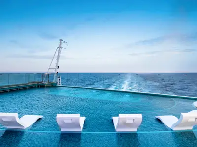 Ein Infinity Pool an Bord der MSC Seashore mit eleganten weißen Lounge-Sesseln im Wasser und einem weiten Blick auf das offene Meer und die Schiffswasserlinie.