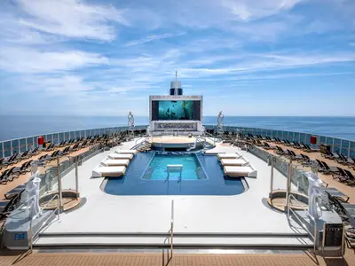 Vogelperspektive auf den Heckbereich der MSC Seashore mit dem Long Island Pool, umgeben von Sonnenliegen und einer grossen Leinwand, die Unterwasserbilder zeigt. Im Hintergrund das offene Meer.