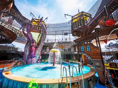 Der Pirates Cove Aquapark an Bord der MSC Seashore: Bunte Wasserrutschen, ein lila Krake und Piratenschiff-Elemente. Ein Pool mit spritzenden Attraktionen im Vordergrund.