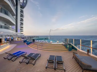 Abendlicher Blick auf den beleuchteten Infinity Pool und das Sonnendeck am Heck der MSC Seashore. Liegestühle auf dem Holzdeck. Im Hintergrund das weite Meer und der Dämmerungshimmel.