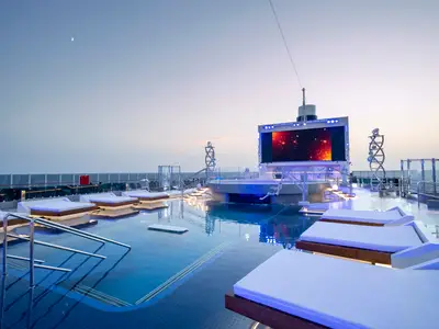 Blick auf den beleuchteten Long Island Pool an Bord der MSC Seashore in der Abenddämmerung. Ein grosser LED-Bildschirm zeigt Sterne. Elegante Liegeflächen sind im Pool und am Rand zu sehen. Eine entspannte Atmosphäre.