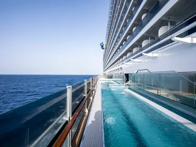 Das Deck der MSC Seashore mit Infinity-Whirlpools, die entlang der Glasbalustrade zum offenen Meer führen. Ein blauer Wasserrutschenturm ist im Hintergrund sichtbar.