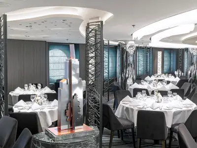 Das elegante Central Park Restaurant an Bord der MSC Seashore. Es zeigt runden, weiß gedeckte Tische mit dunklen Stühlen. Moderne Raumteiler und eine grosse, abstrakte Skulptur schmücken den Raum.