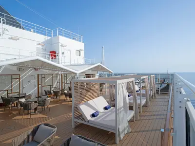 Ein sonniges Deck der MSC Seashore mit komfortablen Liegebetten, stilvollen Cabanas und schattigen Tischen am Meer. Die weisse Reling umgibt den Bereich, unter blauem Himmel.