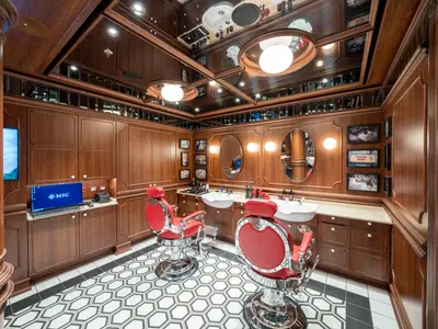 Ein stilvoller Barbershop an Bord der MSC Seashore. Der Raum ist mit dunklem Holz vertäfelt und roten Friseurstühlen ausgestattet. Der Boden hat ein schwarz-weißes Wabenmuster.