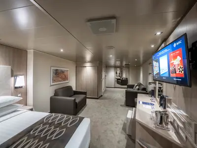Eine moderne Suite an Bord der MSC Seashore. Sie zeigt einen Schlafbereich mit Doppelbett und einen Wohnbereich mit zwei Sofas und grossem Fernseher.