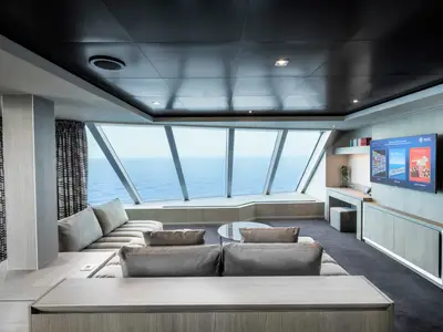 Die luxuriöse Owners Suite der MSC Seashore bietet Panoramafenster mit Meerblick, ein großes Ecksofa, Couchtisch und TV. Die Einrichtung ist modern und elegant.