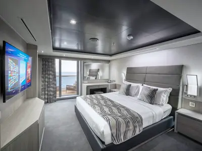 Eine geräumige, elegant eingerichtete Suite an Bord der MSC Seashore mit Doppelbett, TV, Schminktisch und Zugang zu einem privaten Balkon mit Meerblick.