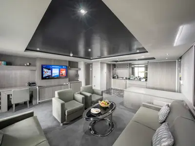 Helle und moderne Royal Suite mit großem Wohnbereich an Bord der MSC Seashore. Sie zeigt bequeme Sofas, einen Schreibtisch und eine integrierte Minibar mit Kaffeemaschine.