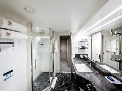 Das luxuriöse Badezimmer einer Suite an Bord der MSC Seashore. Mit moderner Glasdusche, Doppelwaschbecken aus dunklem Marmor und frischen Handtüchern. Elegantes Design, beleuchtet von hellem Licht.